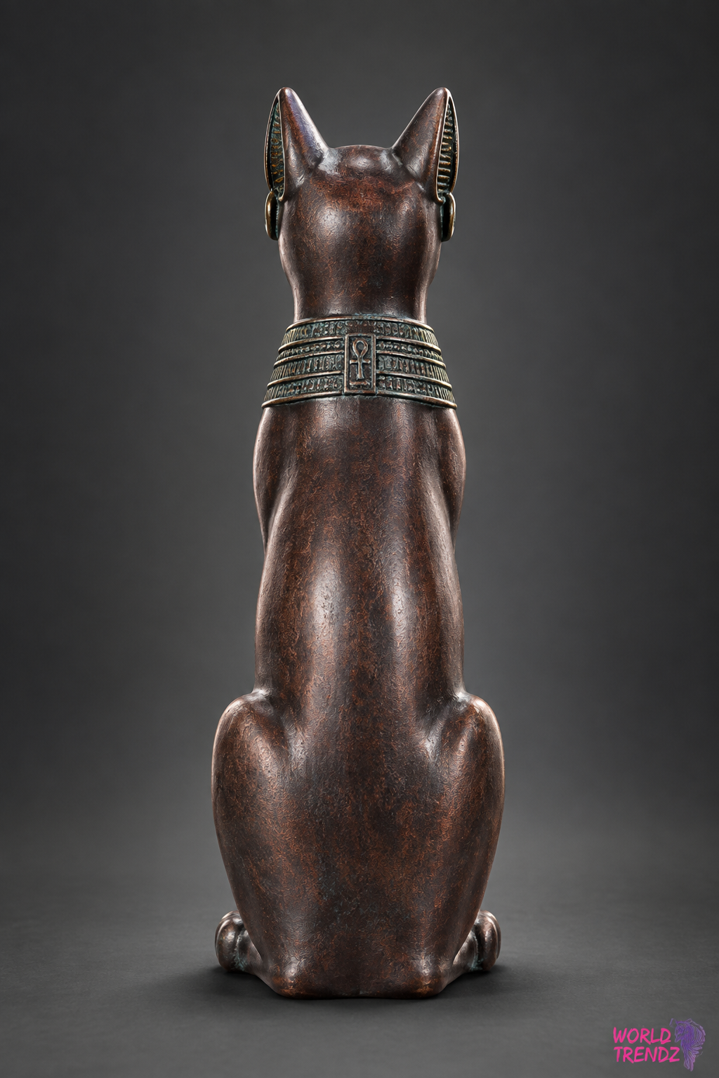 A bronze-finished Egyptian Small Bastet shown from the back, featuring detailed hieroglyphic patterns on its collar and ears, set against a dark gray studio background.