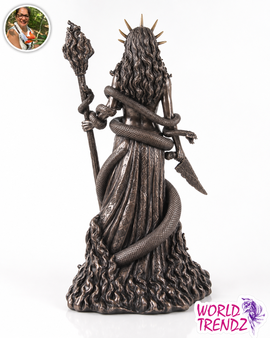A dark metallic bronze statue of Hecate, a crowned woman wrapped in a serpent, holding a staff and a scythe, set against a plain white background. A circular inset photo of a woman is visible in the top-left corner, and a 'WORLD TRENDZ' logo watermark is in the bottom-right corner.
