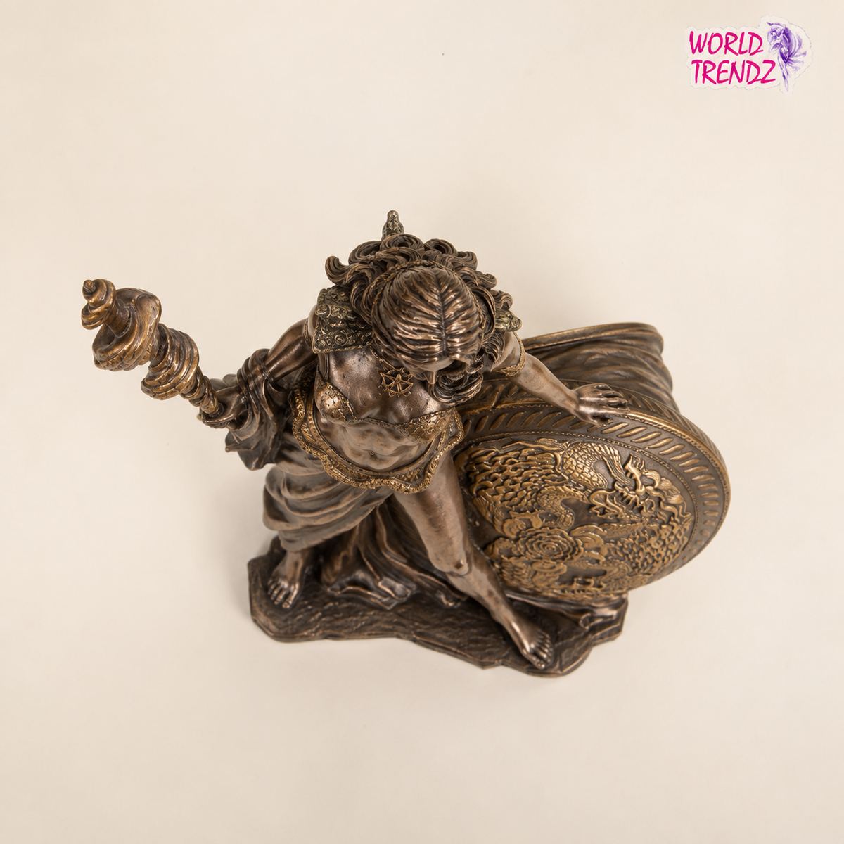 A detailed bronze-finished figurine of a woman Frigga, carrying a large dragon-patterned shield, shown against a plain off-white background with a 'World Trendz' logo in the top right corner.