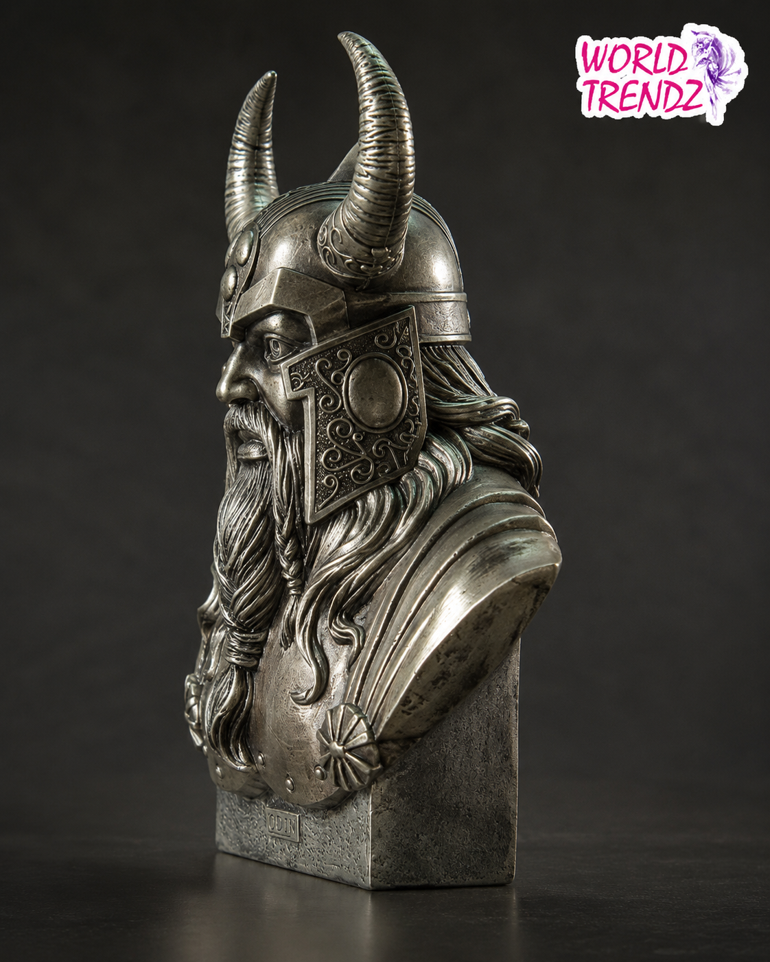 A detailed metal bust sculpture of Odin Cold Cast Bronze Statue wearing a horned helmet and long beard, mounted on a rectangular base against a dark studio background. A 'WORLD TRENDZ' logo appears in the top right corner.