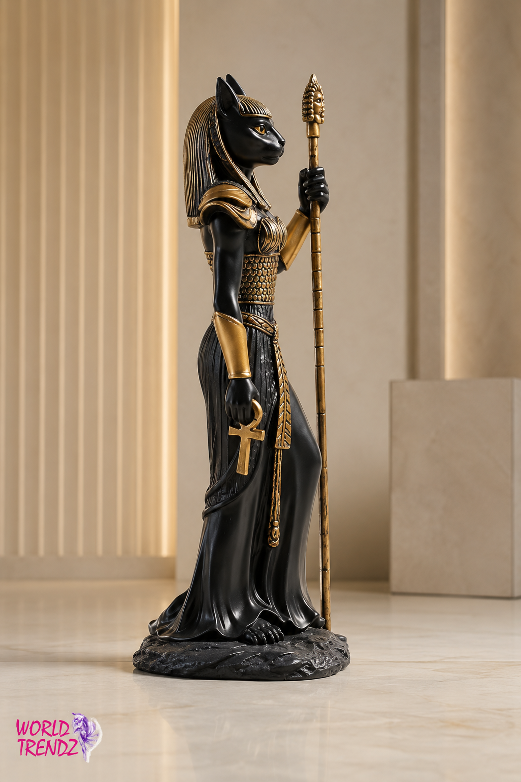 A black and gold statue of an Egyptian Bastet Goddess Statue holding a staff, standing on a base in an indoor setting with beige columns.