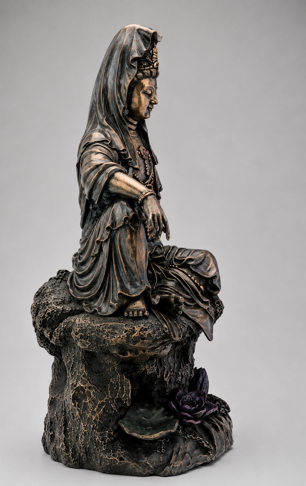 Bronze statue of Guanyin a seated figure on a rock with a gray background