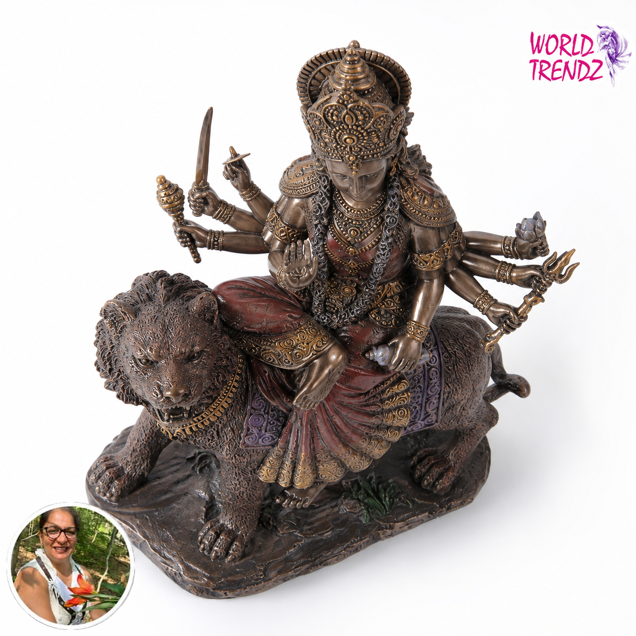 A bronze-finished statue of a multi-armed goddess Durga riding a lion, shown on a plain white background. A pink 'WORLD TRENDZ' logo appears in the top right, and a circular inset photo of a woman is in the bottom left corner.