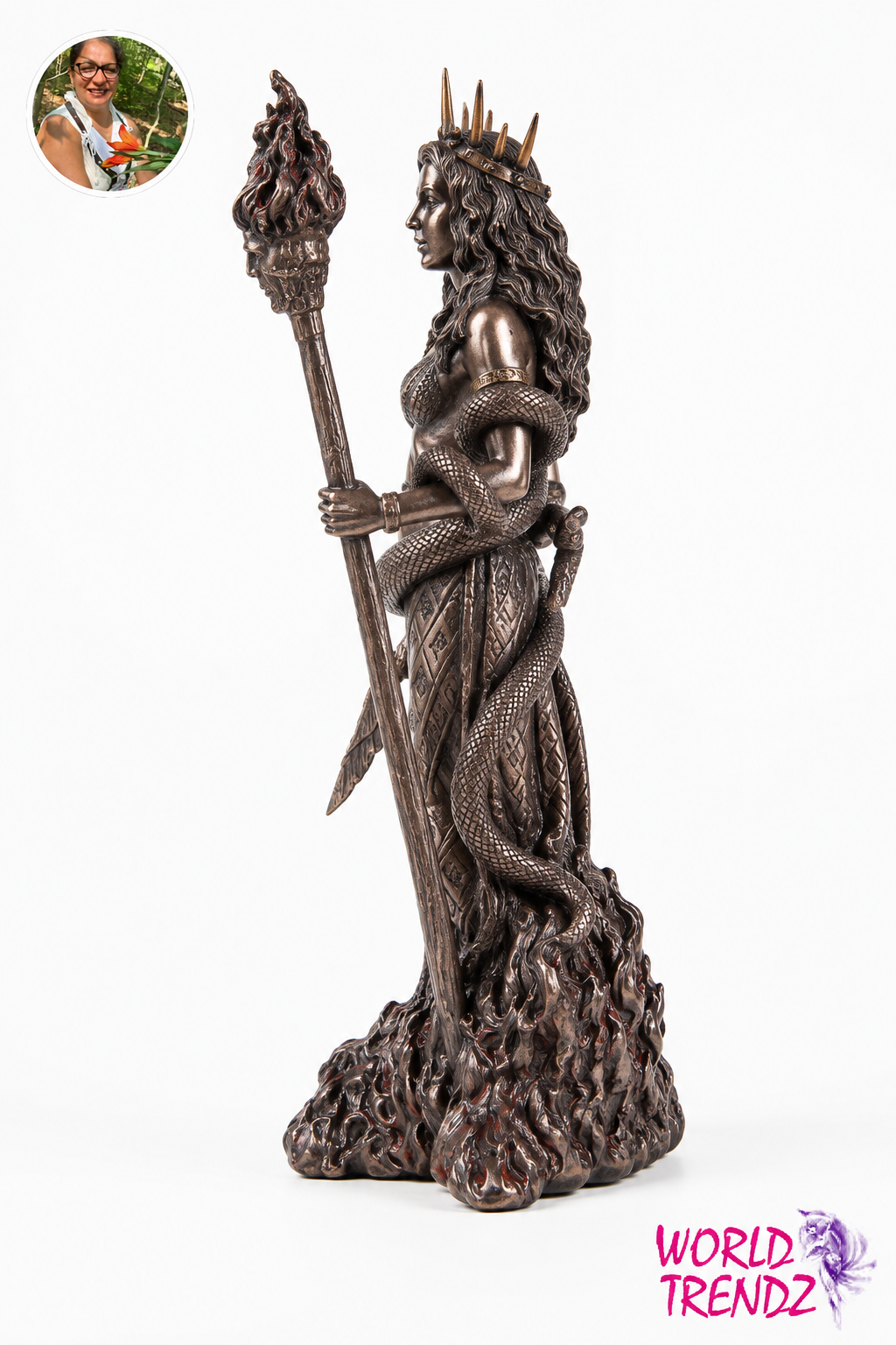 A dark bronze-finished statue of Hecate, a crowned female figure wrapped in a serpent, holding a flaming staff, set against a plain white background. A circular inset photo of a woman appears in the top-left corner, and a 'WORLD TRENDZ' logo is in the bottom-right corner.