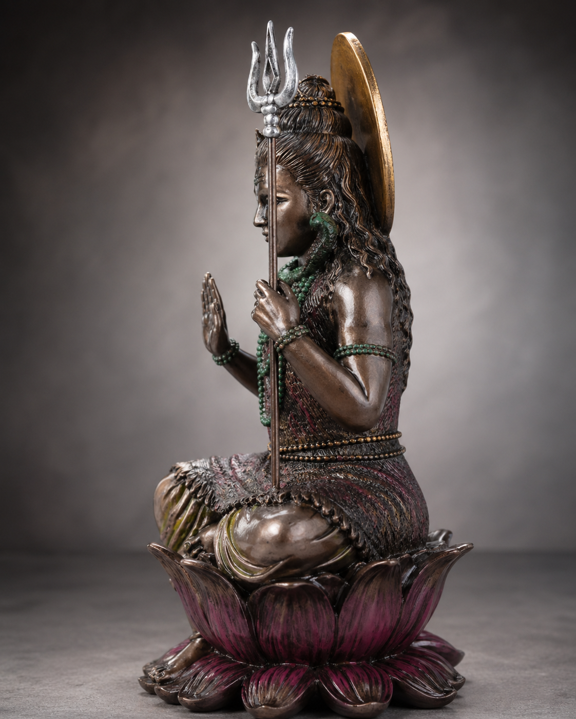 Bronze statue of Shiva with a trident and discus on a lotus flower against a gray background