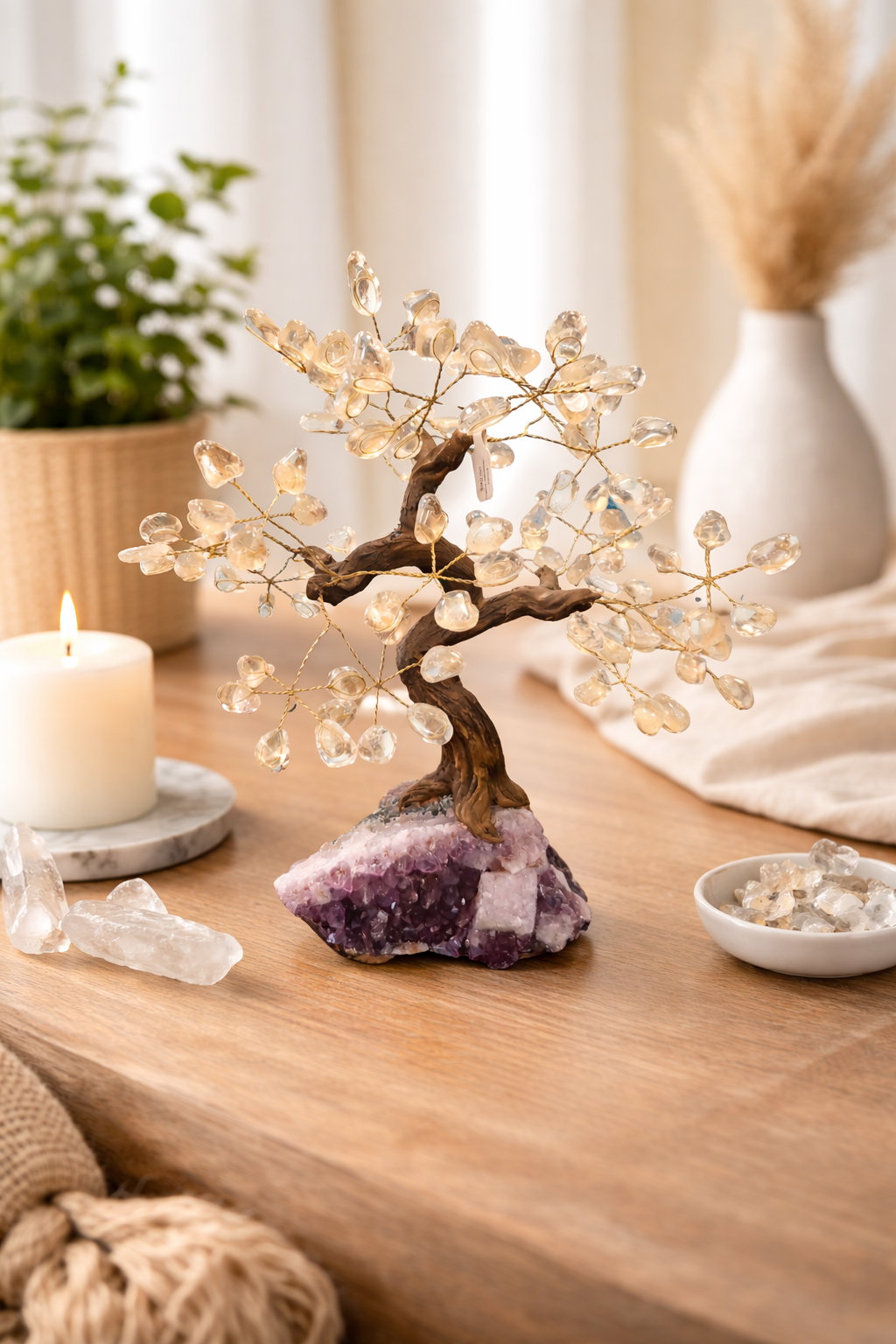 Decorative crystal tree on amethyst base on a wooden surface, surrounded by plants and a candle.