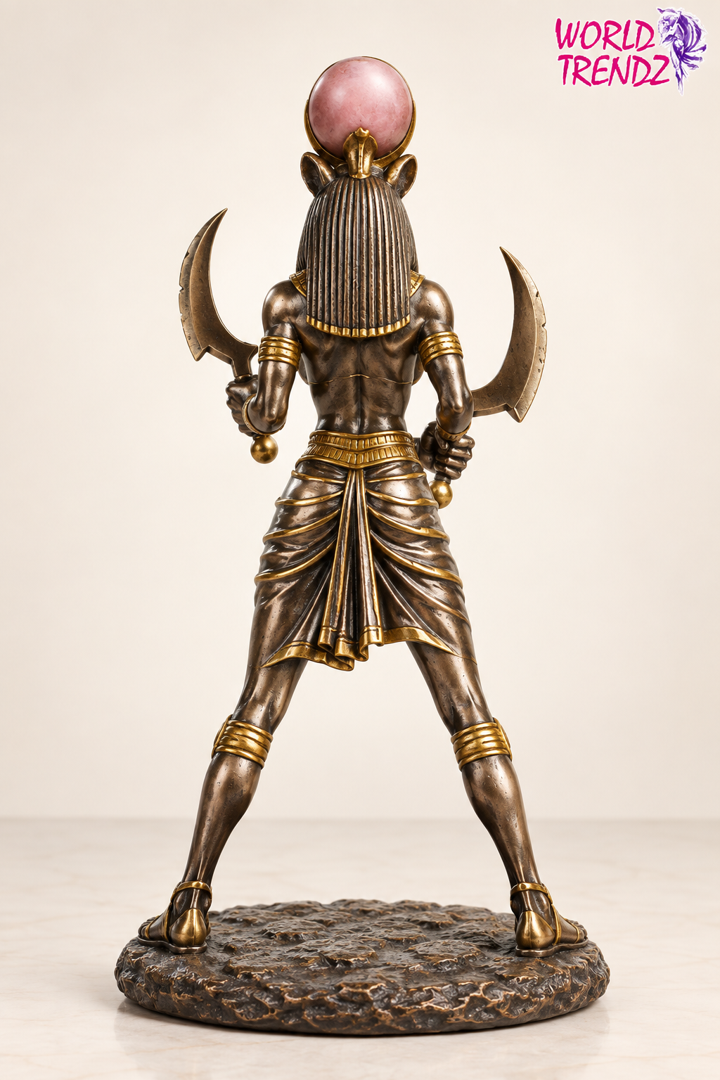 A bronze-finished Egyptian Sekhmet Statue shown from the back, holding two scimiters and wearing a pink cobra headdress, standing on a textured round base against a plain light background.
