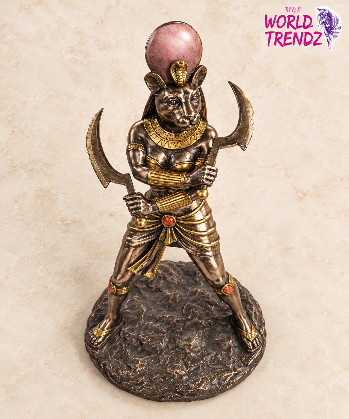 An Egyptian Sekhmet Statue with a bronze finish and gold accents, standing on a textured base with a pink orb on its head, set against a beige background with a 'Star World Trendz' logo in the top right corner.