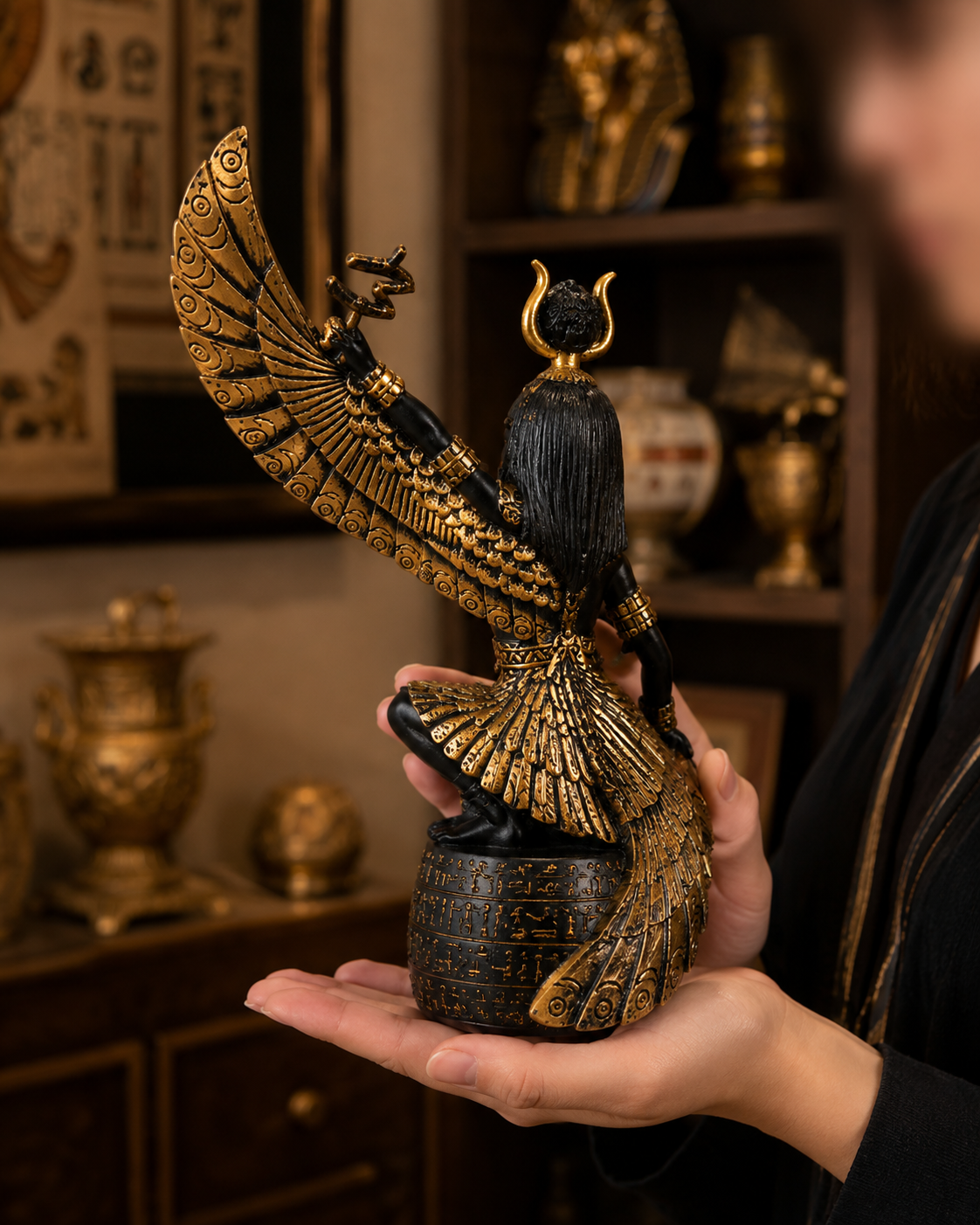 Person holding a detailed figurine of Goddess of Fertility Isis, a winged creature with a headdress in a room with decorative items.