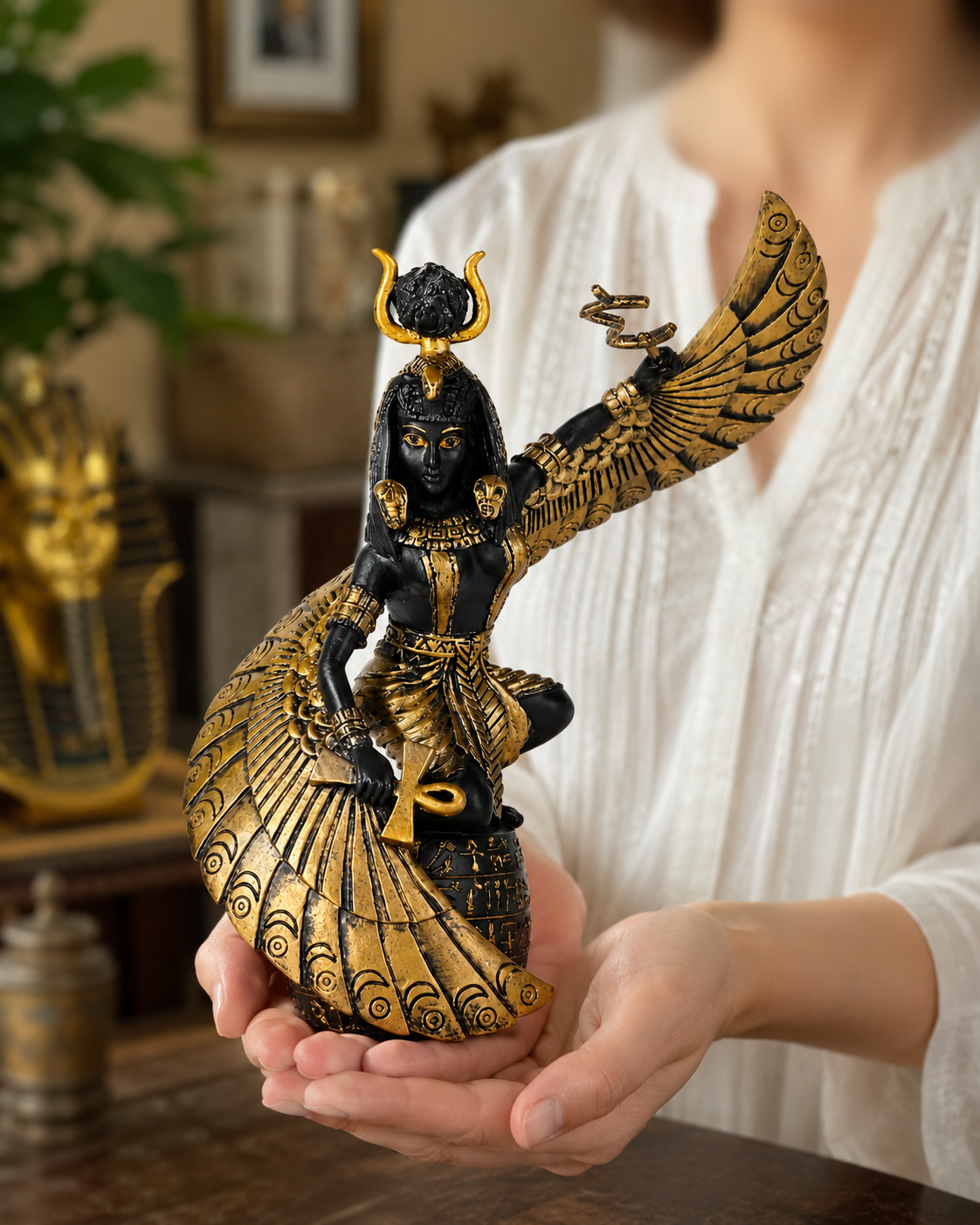 Person holding a decorative figurine of Goddess of Fertility Isis, a winged creature with black and gold details.