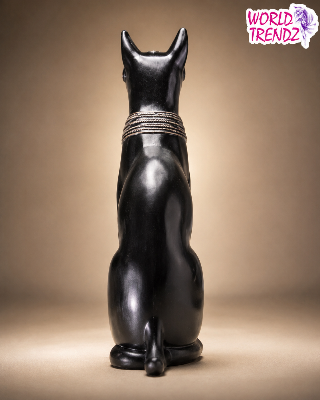 A glossy black cat figurine Bastet shown from the back, wearing a textured gold collar, set against a warm beige gradient background with a 'World Trendz' logo in the top right corner.