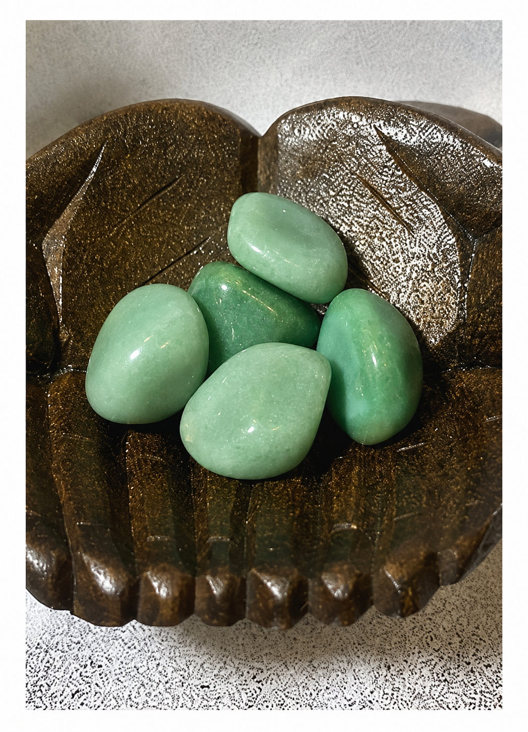 Small collection of polished green aventurine gemstones resting in a carved wooden hand-shaped bowl.
