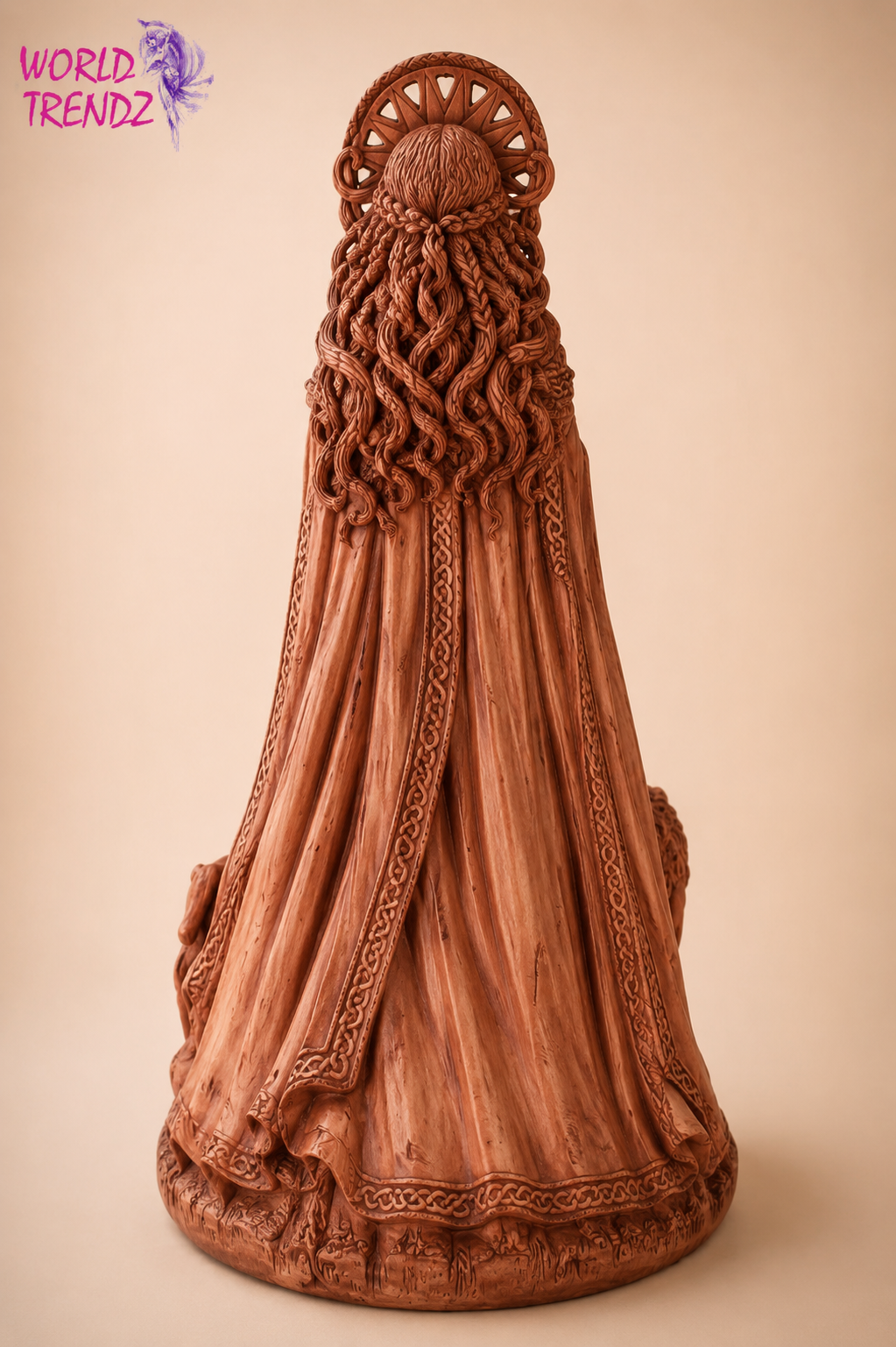 A hand-carved figurine of Goddess Brigid with long, wavy hair and a draped cloak, shown from the back against a solid beige background. A 'WORLD TRENDZ' logo is visible in the top-left corner.