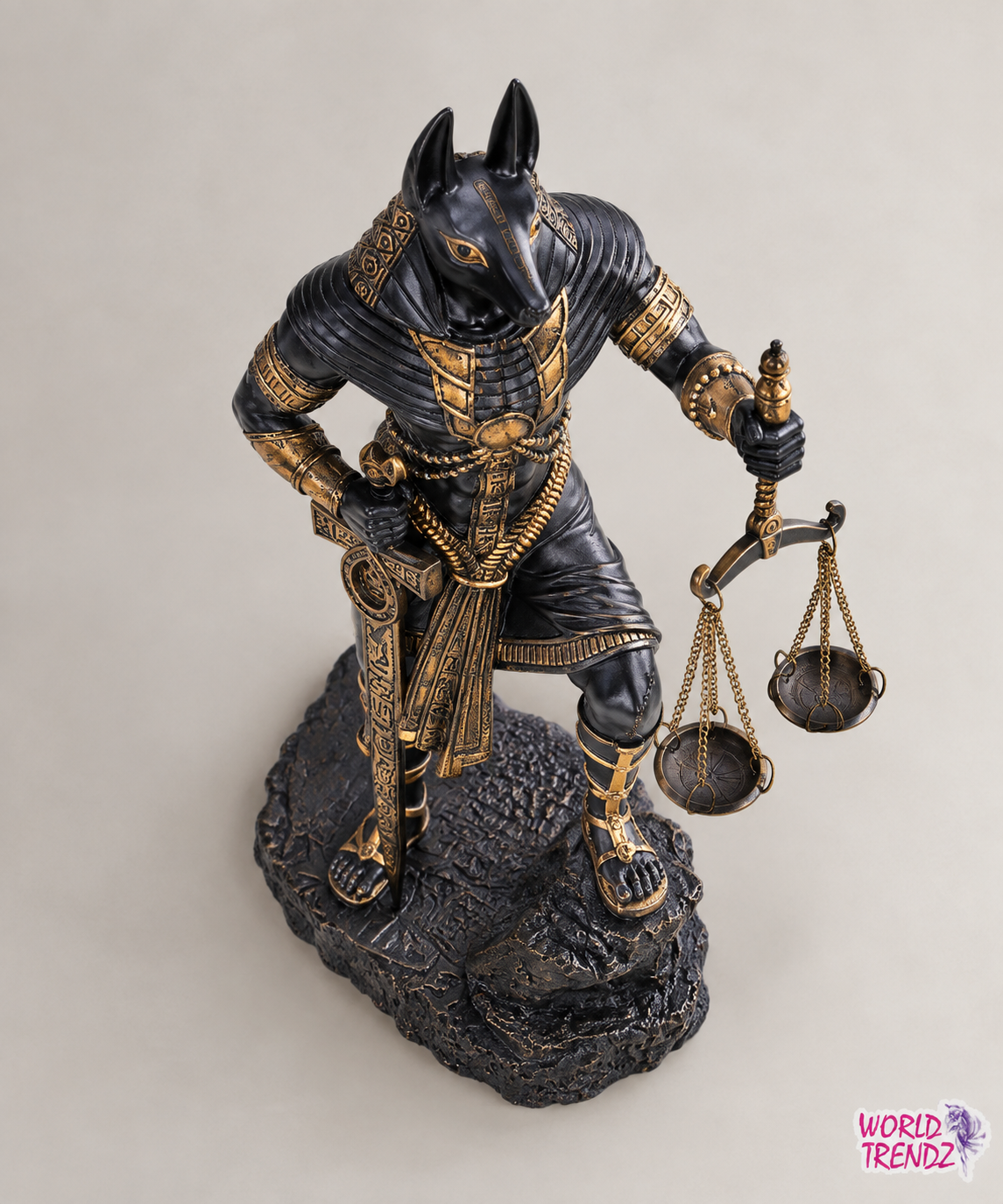 An Egyptian Judgement of Anubis statue representing the god of justice, depicted as a jackalope with a black and gold body, holding a balance scale on a dark textured base against a neutral background.