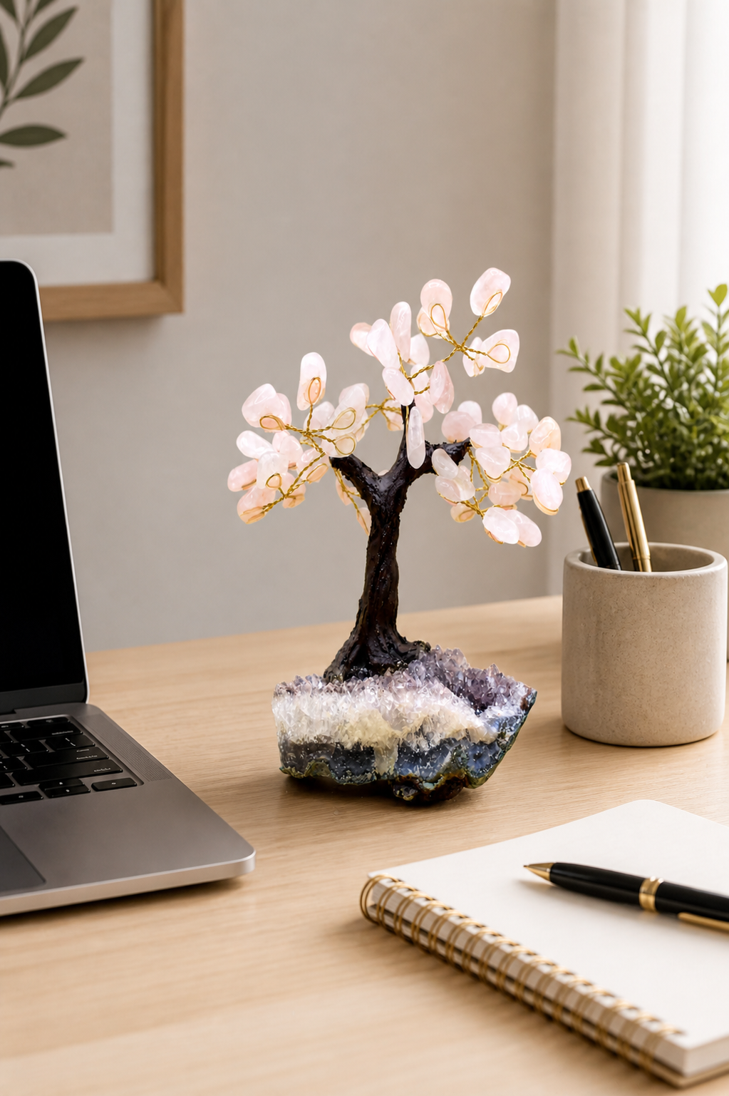 Rose quartz gemstone tree placed on a clean, minimal workspace desk beside a laptop, notebook, and pen holder.