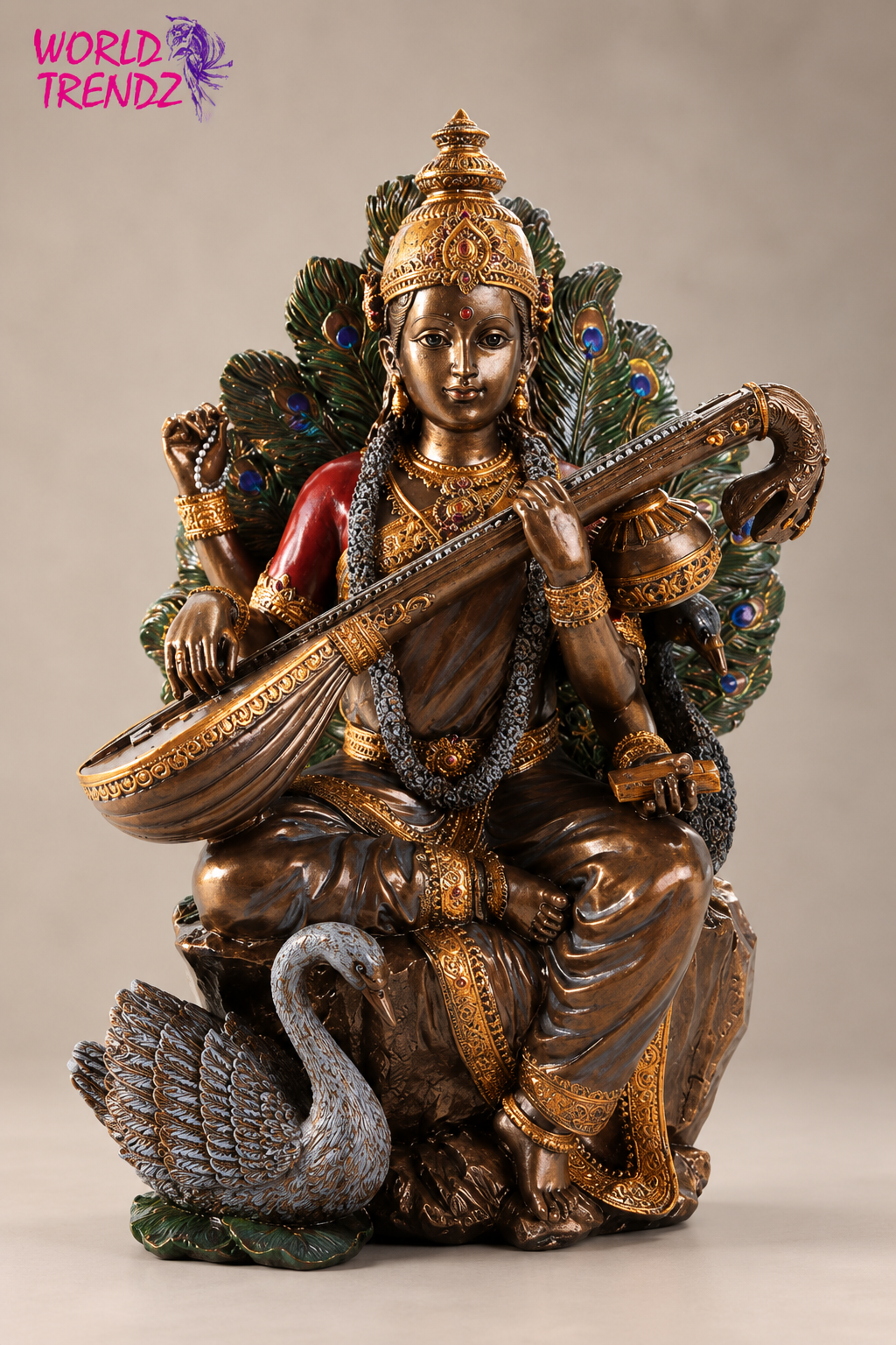 A detailed bronze-finished statue of a Hindu goddess Saraswati seated on a peacock, holding a veena stringed instrument, with peacock feathers behind her and a red garment on one arm, set against a neutral beige background.