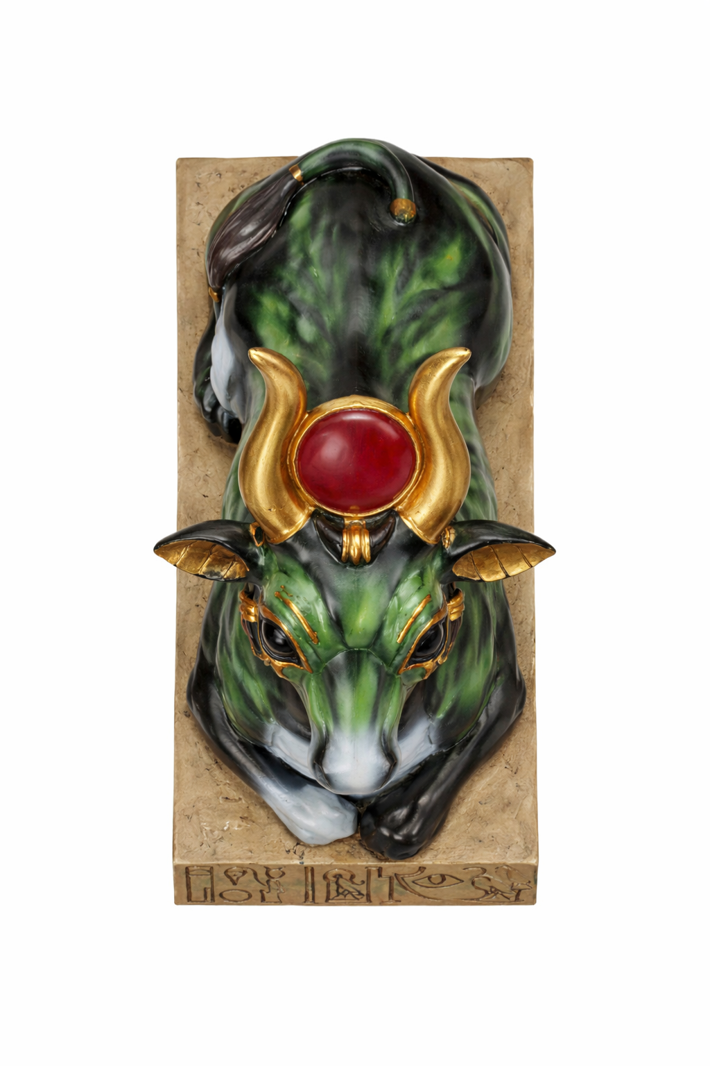 Decorative mask of a green creature with gold accents and a red stone on a cardboard backing.