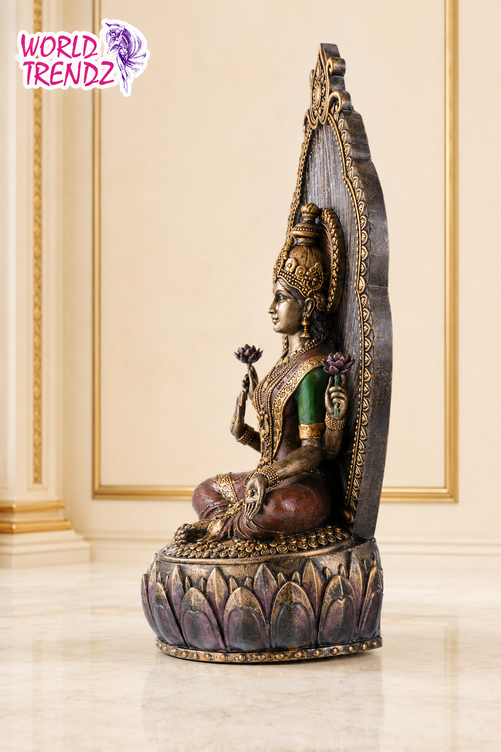 A detailed Lakshmi statue seated on a lotus base, featuring a dark metallic finish with gold accents and a green garment, set against an elegant cream-colored interior background with gold trim.