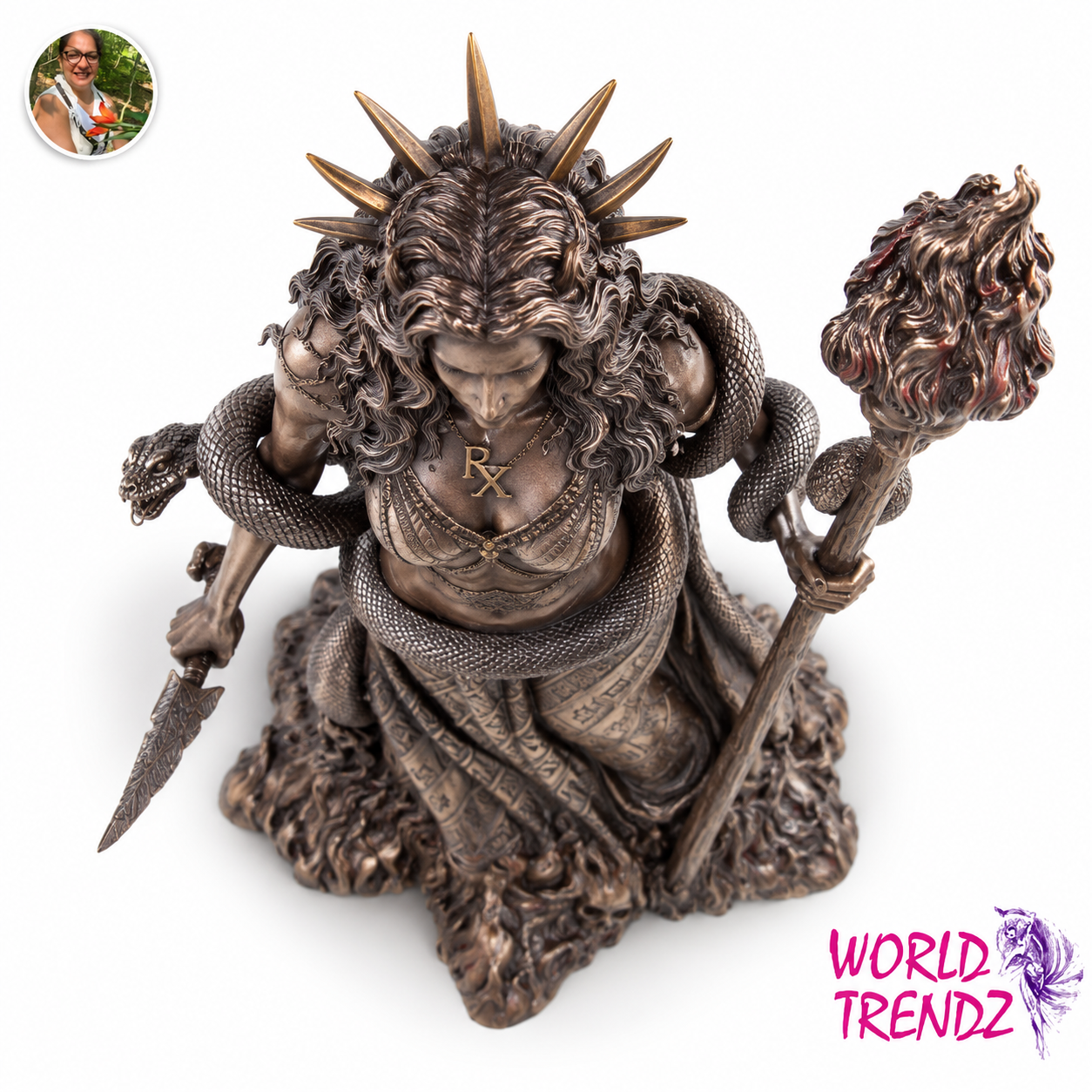 A bronze-finished statue of Hecate, a horned female figure wrapped in snakes, holding a spear and a staff topped with a flame-like form, shown on a plain white background. A small circular inset photo appears in the top-left corner, and a pink 'WORLD TRENDZ' logo appears in the bottom-right corner.