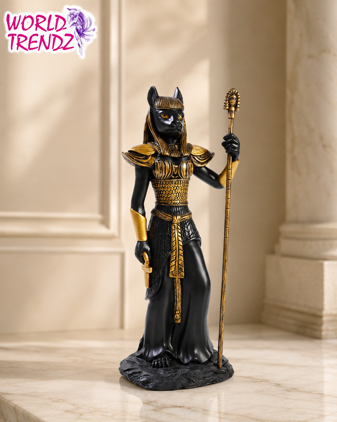 A black and gold Egyptian Bastet Goddess Statue, standing on a marble surface with a classical stone column background. The figurine holds a golden scepter and is detailed with gold patterns on its body and headdress.