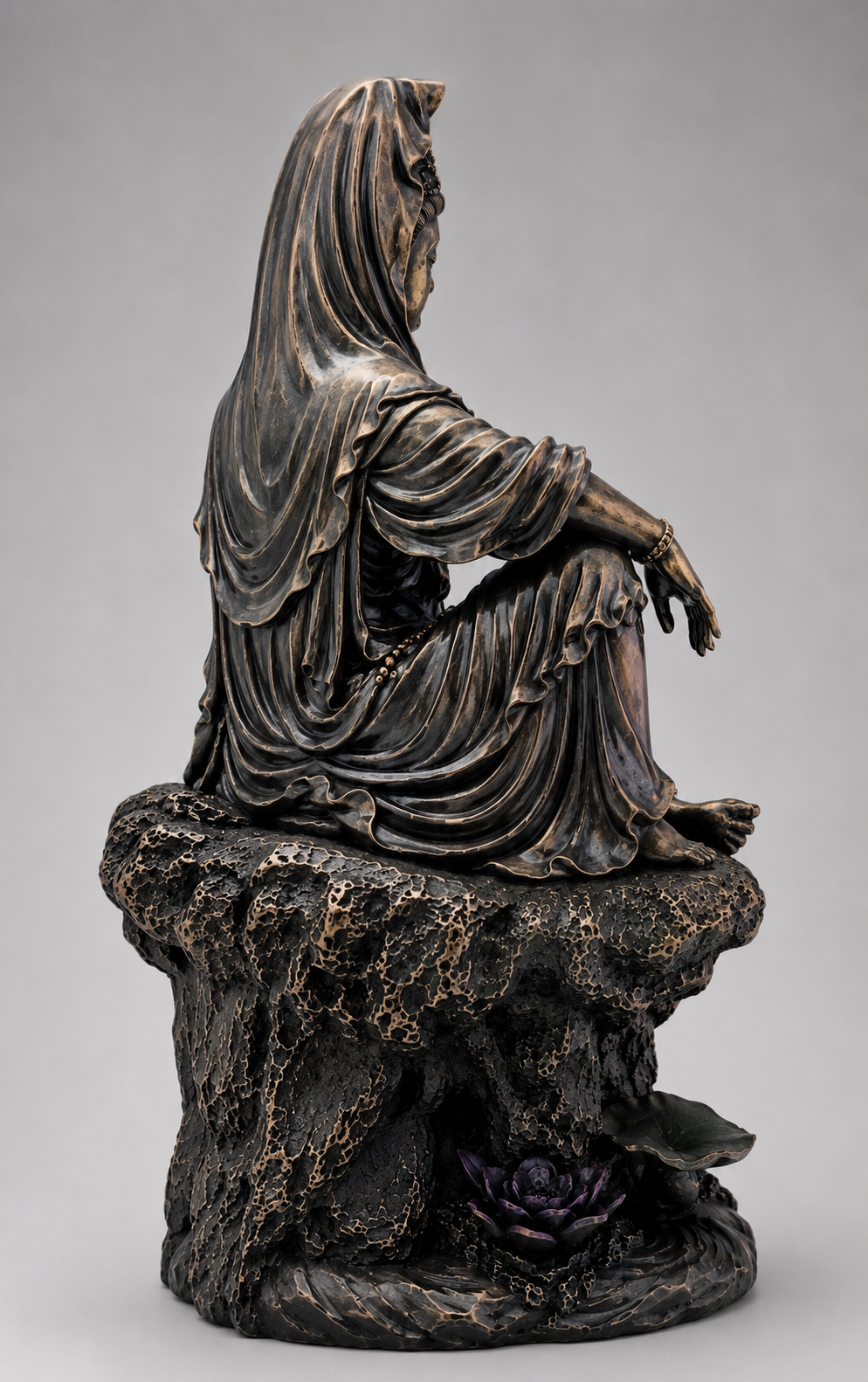 Bronze statue of a seated figure Guanyin with draped garment on a textured base against a gray background