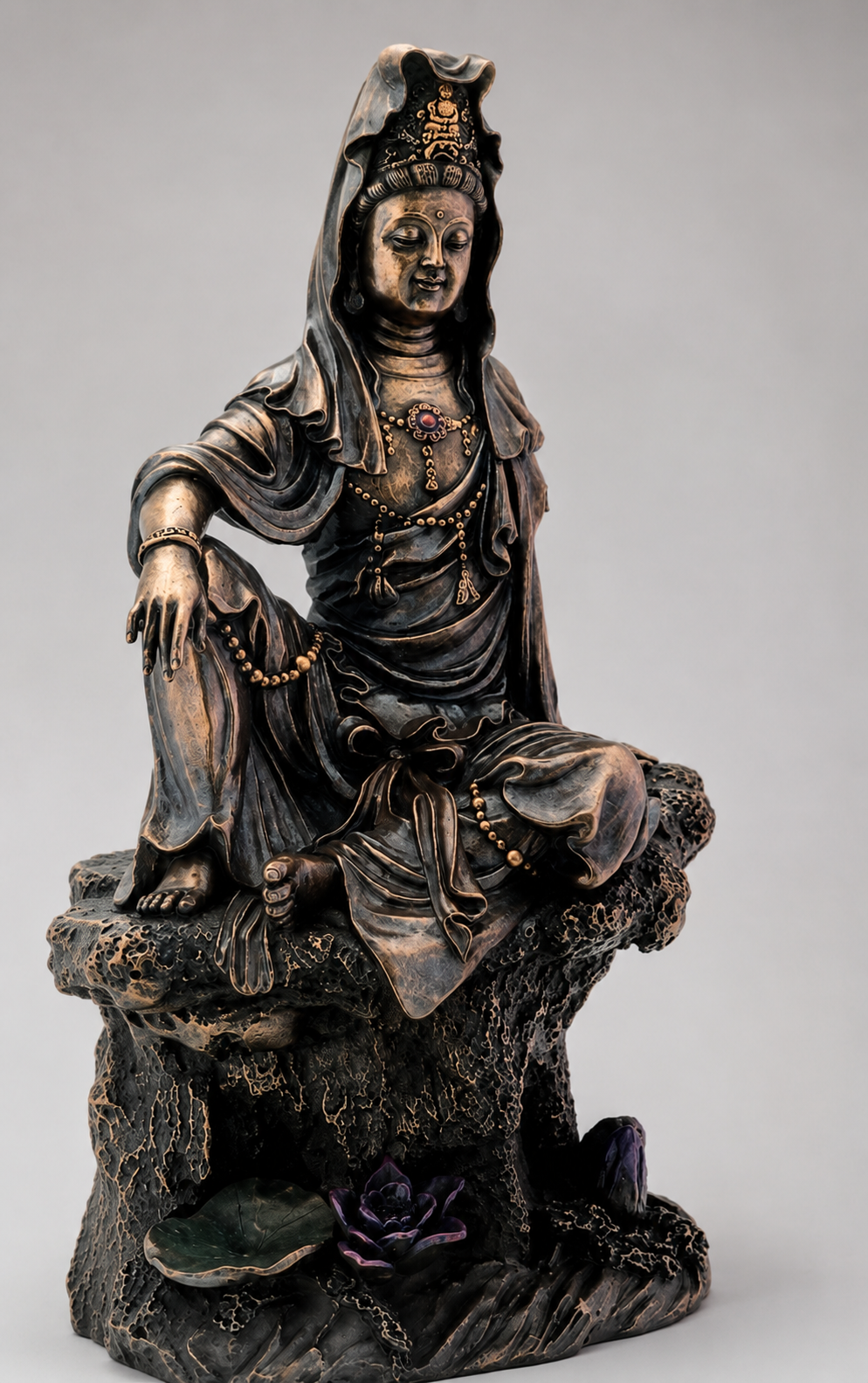 Bronze statue of Guanyin a seated figure on a rock with a plain background