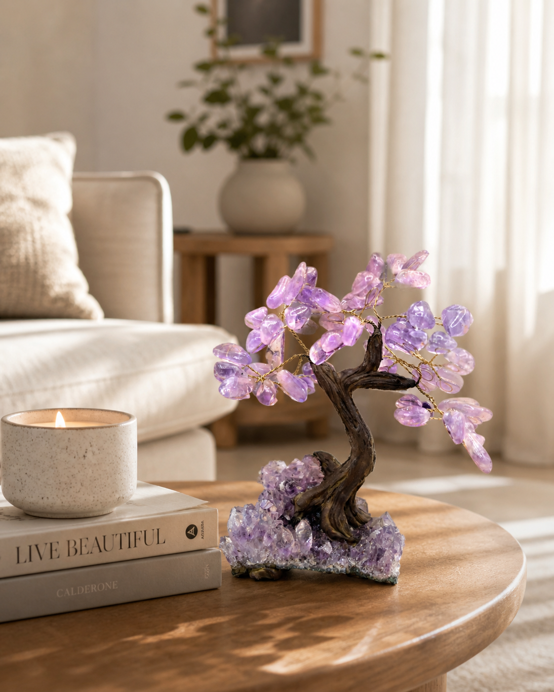 A modern, minimal living room setting with soft neutral tones. The amethyst gemstone tree is placed on a wooden coffee table beside a stack of books and a ceramic candle. Natural sunlight streams through sheer curtains, casting gentle highlights on the crystal leaves. The background remains softly blurred to keep focus on the product. Calm, peaceful, Pinterest-style home aesthetic.
