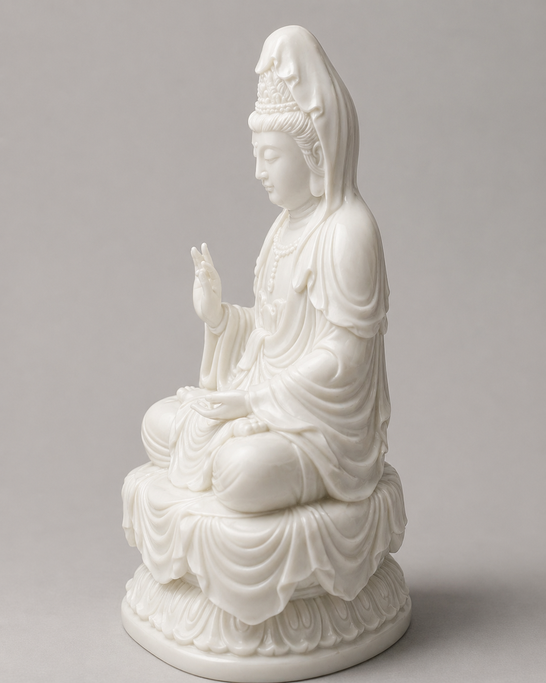 White ceramic statue of a seated Kuanyin on a gray background