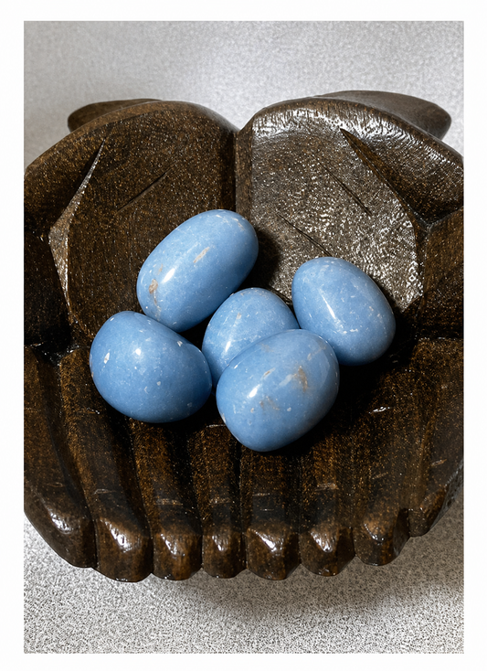Wooden hand with blue Angelite gemstone on a textured gray background